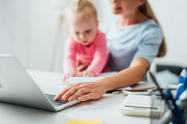 Selective focus of freelancer using laptop and holding baby girl at table 