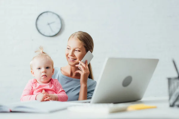 Enfoque Selectivo Mujer Hablando Teléfono Inteligente Mientras Trabaja Cerca Hija — Foto de Stock