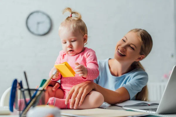 選択的焦点の母見ますの赤ちゃん女の子保持スティッキーノートパソコンの近くにテーブルの上 — ストック写真