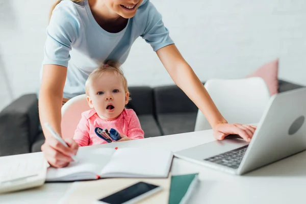 Selective Focus Woman Using Laptop Writing Notebook Infant Daughter Stapler — Stock Photo, Image