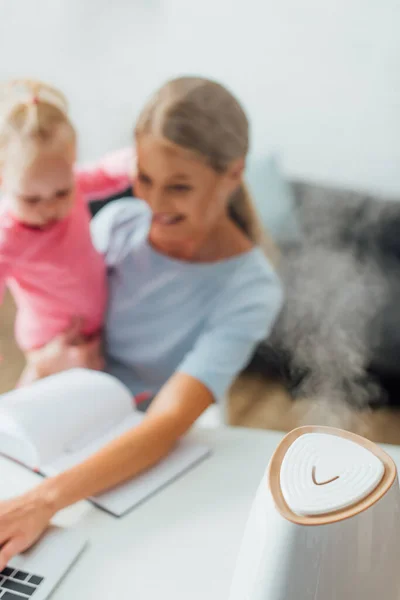 赤ちゃんの女の子を保持し 背景にラップトップを使用して 母親と加湿器の選択的な焦点 — ストック写真