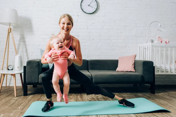 Sportswoman doing lunges on fitness mat and carrying baby daughter — Stock Image Sportswoman Doing Lunges Fitness Mat Carrying Baby Daughter Royalty Free Stock Photos