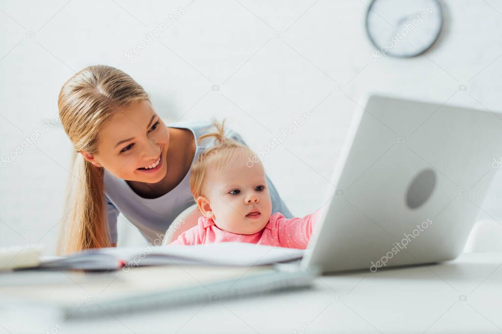 Selective focus of mother standing near kid looking at laptop and stationery on table 