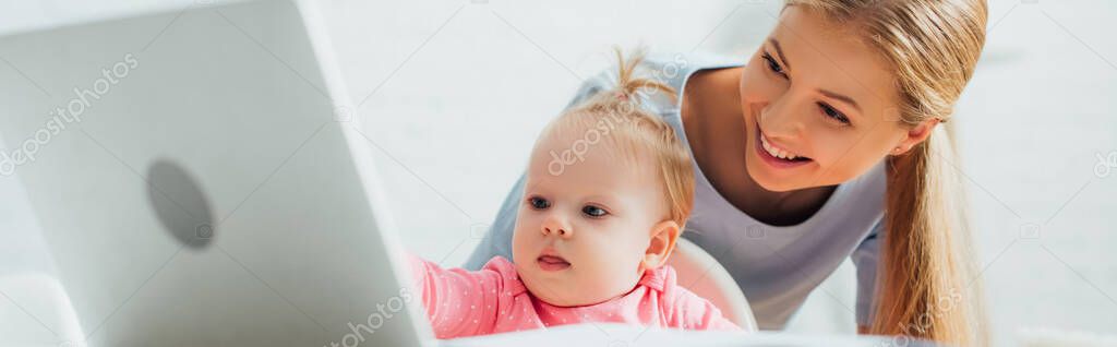 Panoramic crop of infant girl looking at laptop near mother at home 