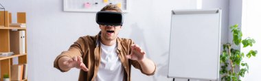 Ağzı açık genç iş adamının iş yerinde vr kulaklık ve jest kullanarak yatay görüntüsü