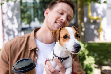 Jack Russell Terrier köpeği ve kahve tutan genç adamın seçici odak noktası. 