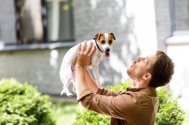 Genç adam dışarıda dururken Jack Russell Terrier köpeği yetiştiriyor.