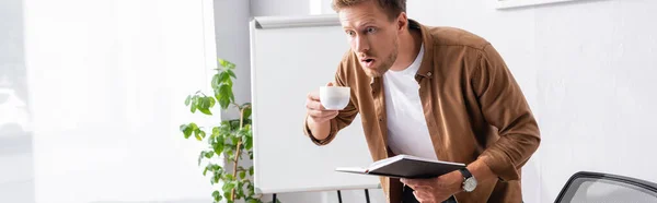 Ofisinde Kahve Fincanı Defteriyle Şok Olmuş Adamının Yatay Görüntüsü — Stok fotoğraf