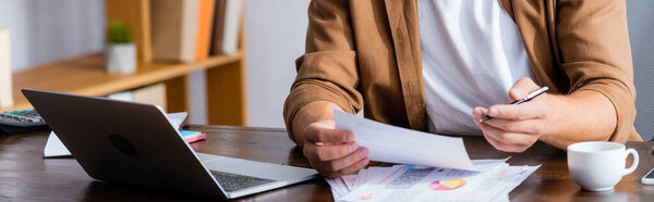 cropped view of businessman working with papers near laptop, horizontal image