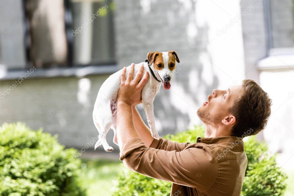 young man raising jack russell terrier dog on hands while standing outdoors