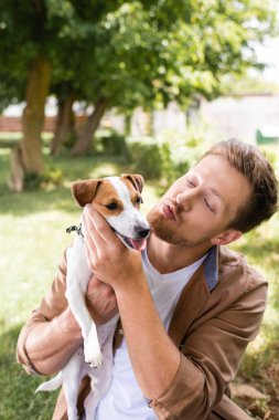 Jack Russell Terrier 'ı parkta tutarken ördek suratı yapan genç adam.