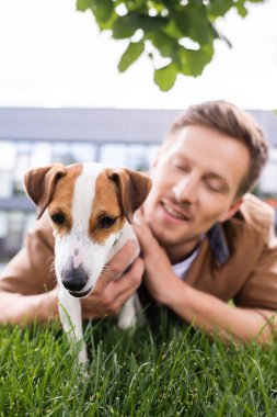 Jack Russell Terrier köpeğiyle yeşil çimlere uzanan genç adamın seçici odak noktası