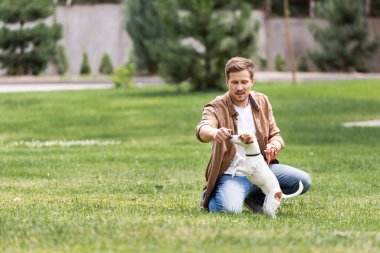 Çimlerde Jack Russell Terrier 'la oynayan genç adamın seçici odak noktası 