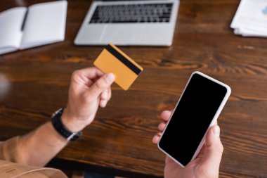 Ofiste çalışırken akıllı telefon ve kredi kartı tutan işadamlarının seçici odak noktası 
