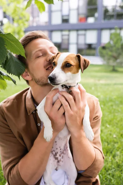 目を閉じた若者が白いジャック ラッセル テリア犬を頭の上に茶色の斑点で — ストック写真