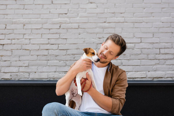 Young man embracing jack russell terrier near building on urban street 