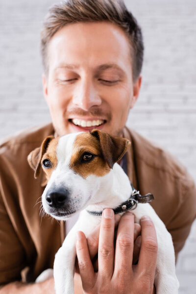 Selective focus of man hugging jack russell terrier looking at camera near building 