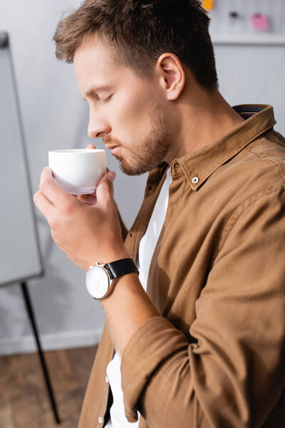 Selective focus of young businessman holding coffee cup in office 