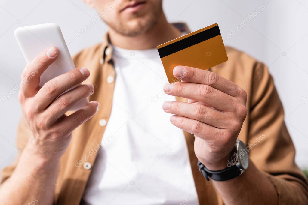 Selective focus of businessman holding credit card while using smartphone in office 