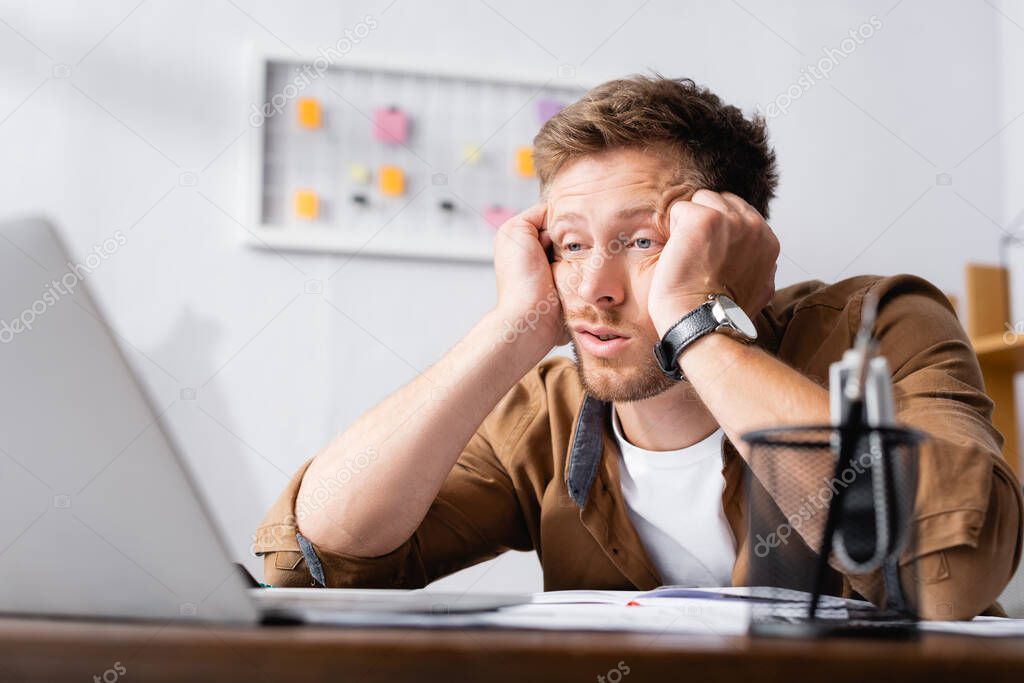 Selective focus of exhausted businessman looking at laptop in office  