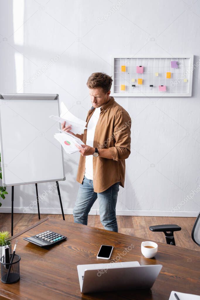 Selective focus of businessman working with documents near gadgets and coffee on table in office 