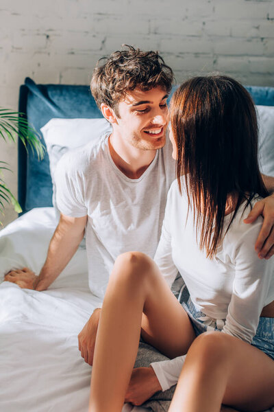 Young couple in pajamas sitting on bed and looking at each other