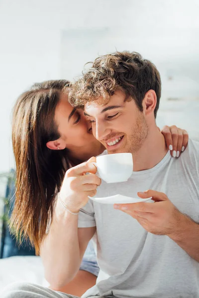 Young woman whispering in ear and touching boyfriend with cup of coffee