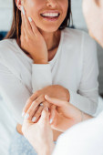 Cropped view of man wearing engagement ring on finger of girlfriend at home 