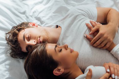Yatakta gözleri kapalı kucaklaşan genç çiftin en iyi görüntüsü. 