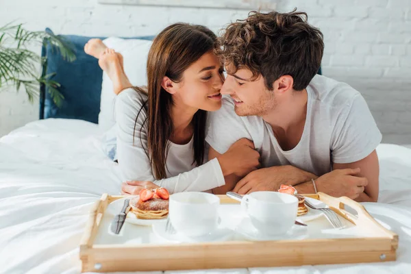 ベッドの上でトレイの上で朝食の近くに横たわる若いカップルの選択的な焦点 — ストック写真