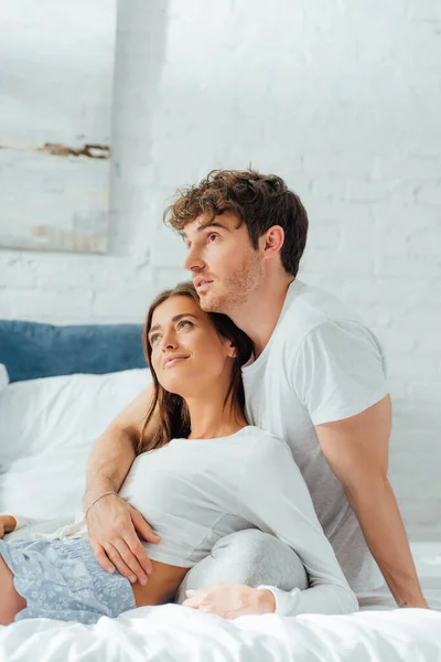 Young man hugging girlfriend in pajamas on bed at morning