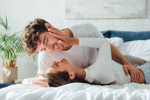Young woman touching face of boyfriend while lying in pajamas on bed 