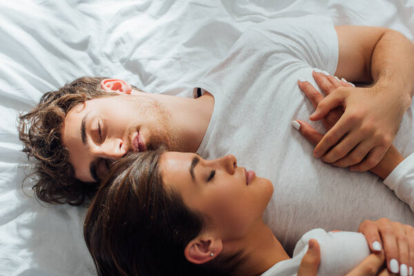 Top view of young couple embracing with closed eyes on bed 