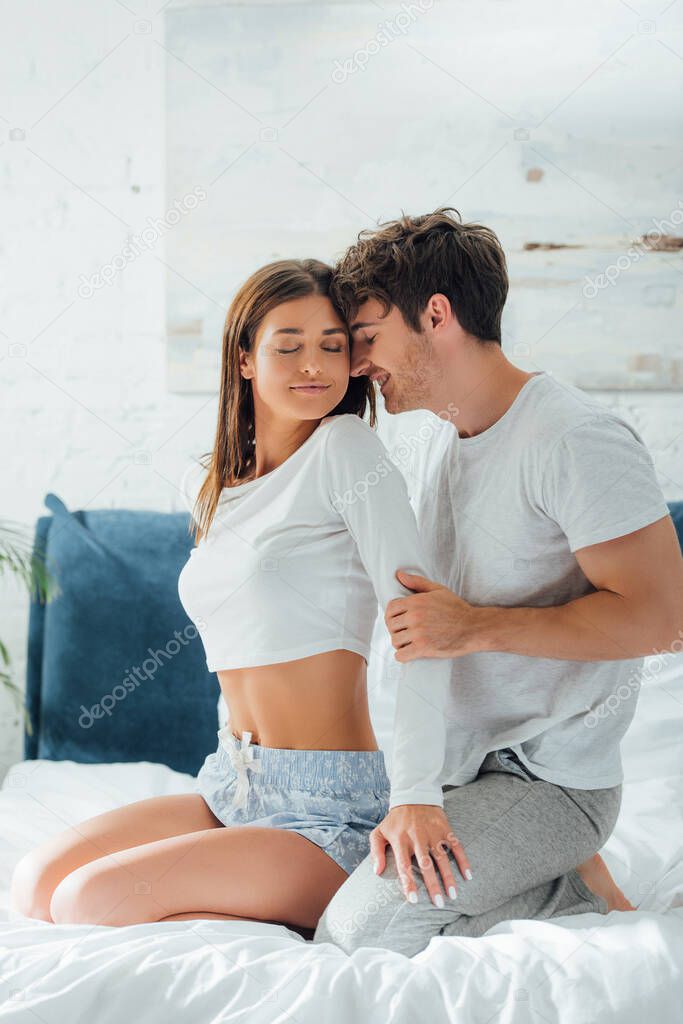 Woman in pajamas touching boyfriend on bed at morning 