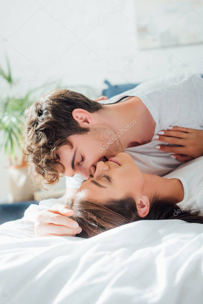 Selective focus of man kissing girlfriend on bed at morning 