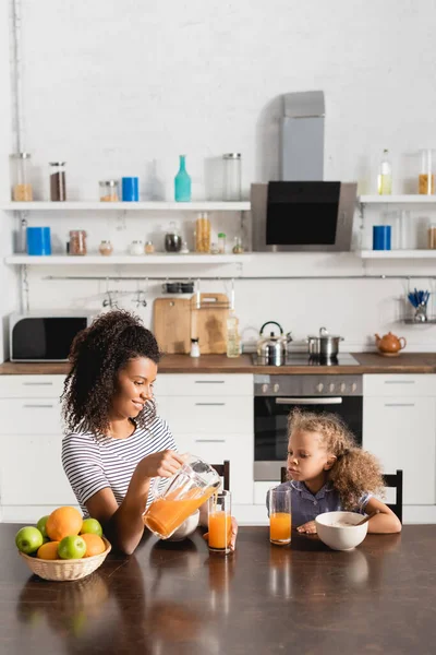 Giovane Donna Afroamericana Versando Succo Arancia Vicino Figlia Frutti Maturi — Foto Stock