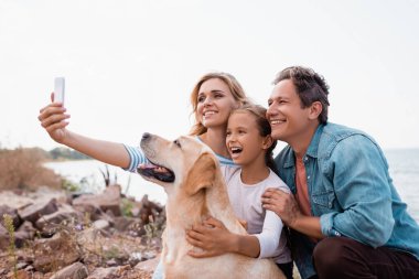 Golden Retriever plajında selfie çeken ailenin seçici odak noktası. 