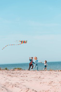 Tatil sırasında kumsalda koşan uçurtmalı ailenin seçici odağı 