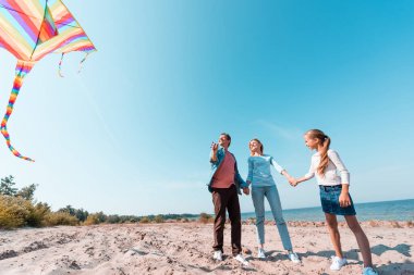 Deniz kenarında uçurtma tutan bir adam, karısı ve kızının yanında. 