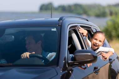 Selective focus of excited girl looking through window of car near father  clipart
