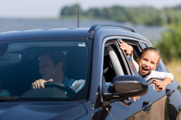 Selective focus of excited girl looking through window of car near father 