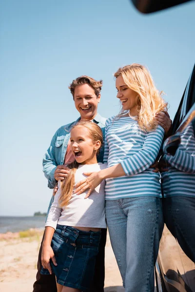 Selective focus of family hugging near auto on beach