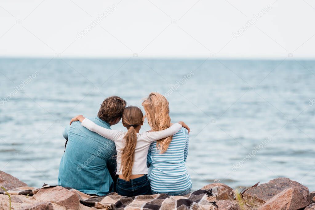 Back view of daughter embracing parents on seaside 