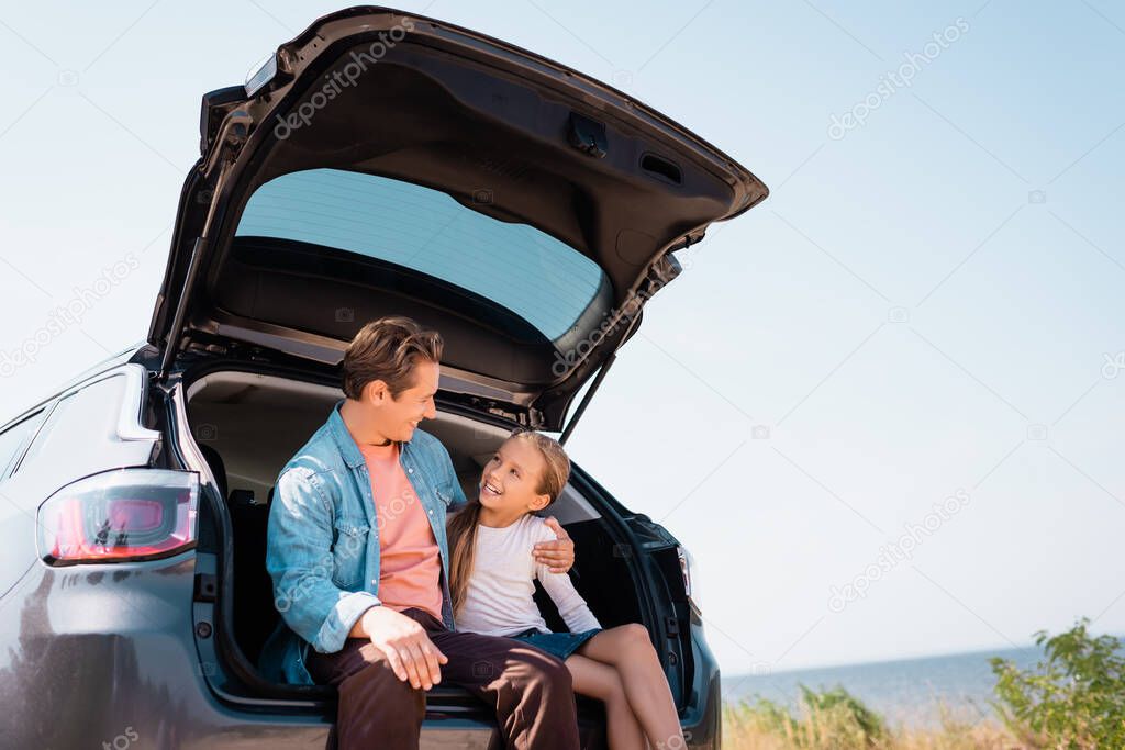 Father hugging child while sitting in trunk of auto on beach 