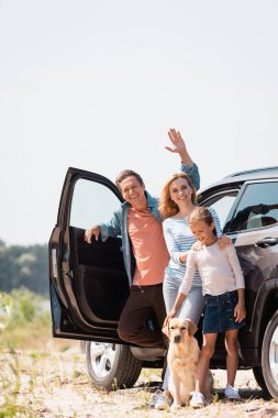 Golden Retriever ve otomobille ailenin yanında el sallayan adamın seçici odak noktası. 