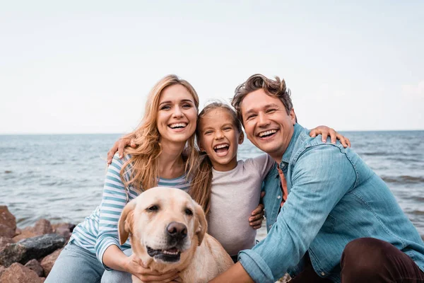 Família Com Golden Retriever Olhando Para Câmera Enquanto Abraça Praia — Fotografia de Stock
