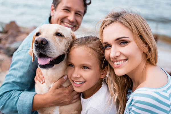 Селективный фокус женщины, смотрящей в камеру рядом с семьей и золотистым ретривером на берегу моря 