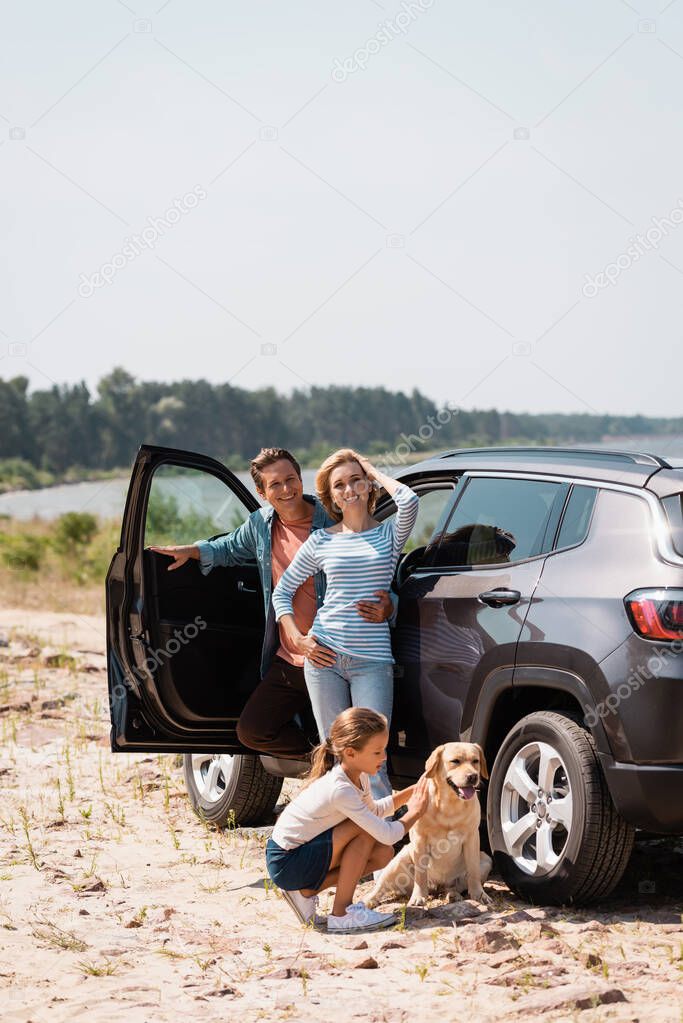 Family with golden retriever looking at camera near car outdoors 