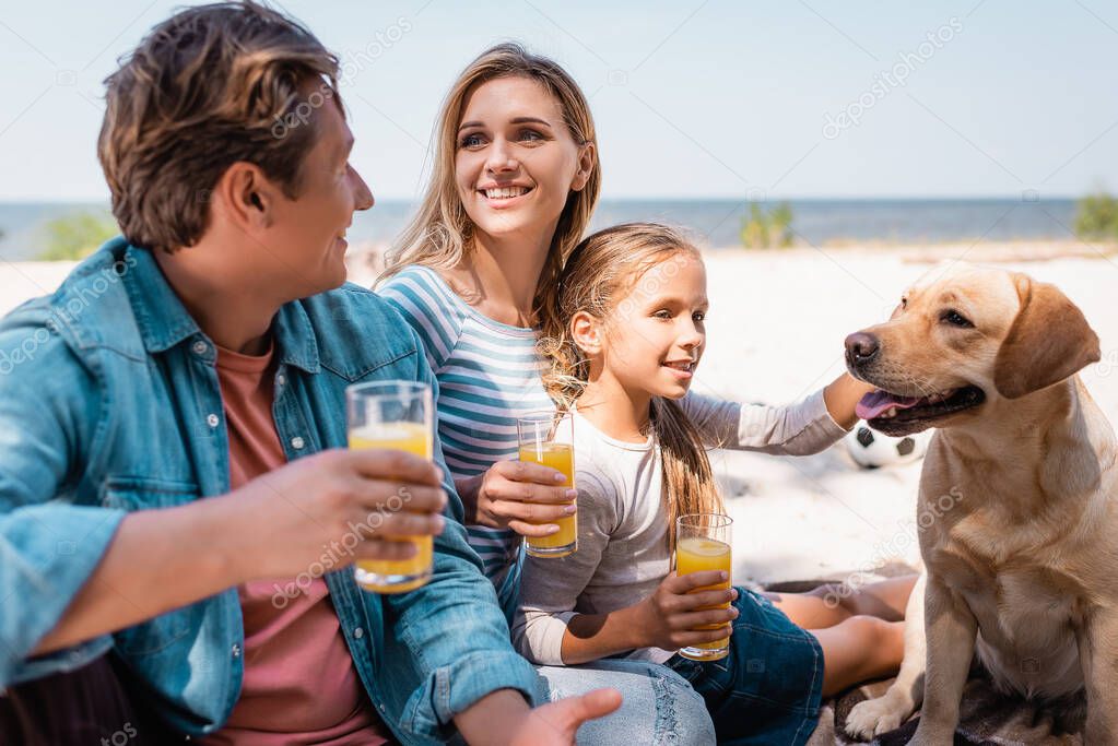 Selective focus of family with golden retriever holding orange juice on beach 