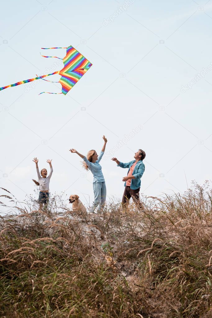 Selective focus of family with golden retriever and kite standing on grassy hill